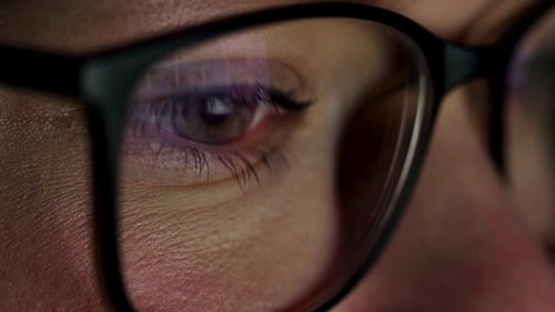 Frau mit Brille schaut auf den Monitor und surft im Internet. Der Monitorbildschirm spiegelt sich im