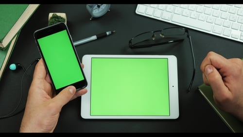 Mann hält Smartphone mit grünem Bildschirm über einen Tisch mit grünem Bildschirm und scrollt etwas darauf