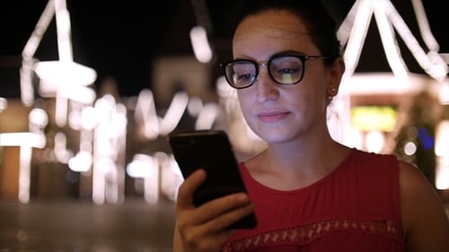 Attractive Girl Using a Mobile Phone While Walking Through the Streets in a Night City