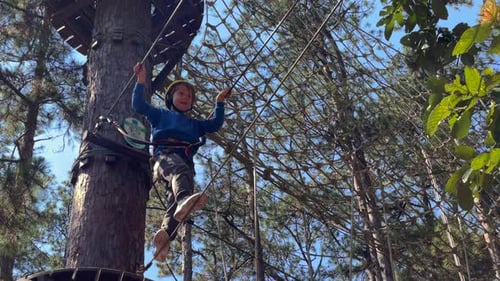 Slowmotion Shot of a Boy in a Yellow Helmet That is Having Fun in a Rope Climbing Adventure Park