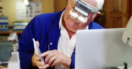 Senior Man Working on Laptop with Magnifying Glass