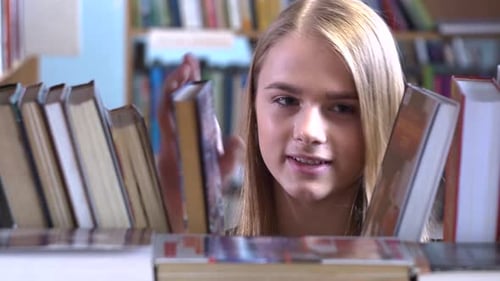 Pretty Young Girl Chooses a Book in the Library