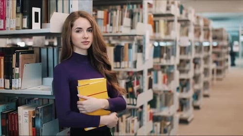 Girl with Long Hair Smiles Standing Before the Shelves in the Library