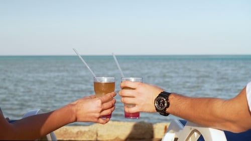 Young Family Couple Sunbathing and Drinking Colored Cocktail at Tropical Beach. Lovers on Honeymoon