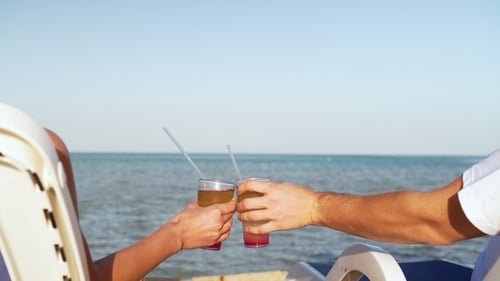 Young Family Couple Sunbathing and Drinking Colored Cocktail at Tropical Beach. Lovers on Honeymoon