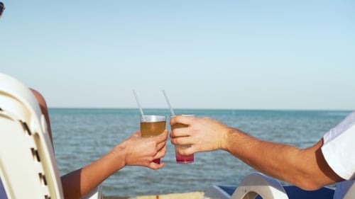 Young Family Couple Sunbathing and Drinking Colored Cocktail at Tropical Beach. Lovers on Honeymoon