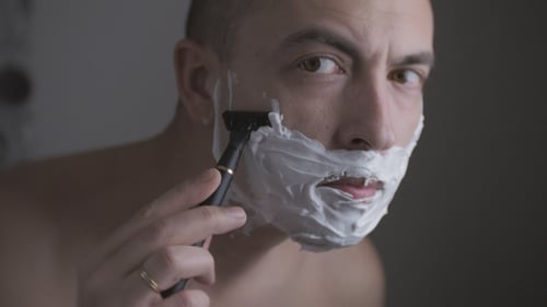 Homme se rasant le visage avec un rasoir à l'aide d'une mousse spéciale