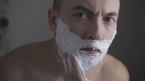 Homem adulto fazendo a barba com espuma e Razer manual