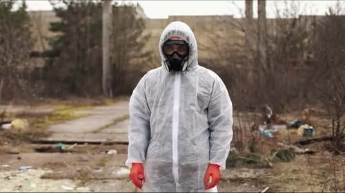 Man in Bio-hazard Suit and Gas Mask Stands Before the Factory
