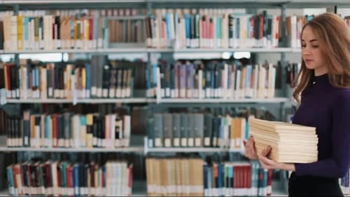 Smiling Female Student Hold Books Walking Before the Shelves in the Library