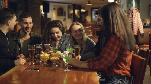 Friends Sharing a Phone at Bar Table