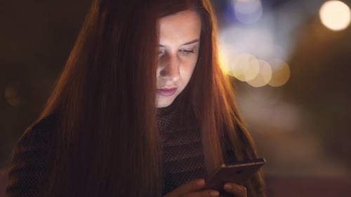 A Woman Is Using a Mobile Phone. Night City. Blurred Background.