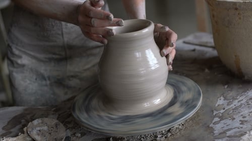 Hands shaping clay into a pot on a wheel
