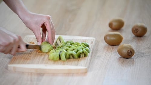 Woman Cutting Kiwi on a Wooden Cutting Board