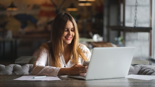 Woman Uses Smartphone and Laptop at Table