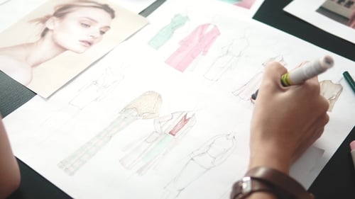 Fashion Designer Sketches Dress Designs at Desk
