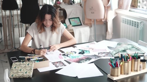 Designer of Clothes Makes a Sketch of Clothes in a Sewing Workshop. a Girl Working for Herself Is