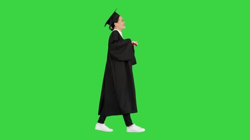 Happy Female Student in Graduation Robe Walking and Cheering with Her Diploma on a Green Screen