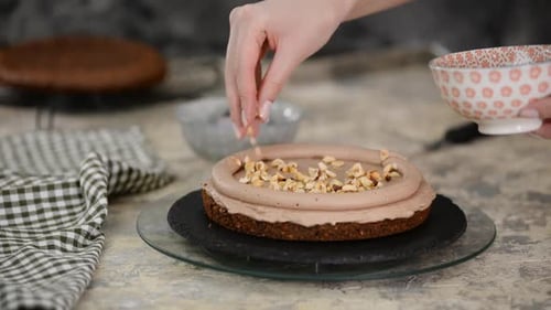 Woman Decorating Chocolate Cake with Nuts