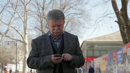 Expirienced Man with Mustache Goes and Surfs the Net on a Phone in Spring