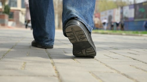 Männliche Füße in schwarzen Schuhen gehen im Frühjahr auf einem Bürgersteig der Stadt