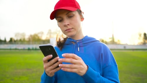 Woman with Wireless Headphones and Smartphone Chooses Music and Runs Through the Stadium at Sunset