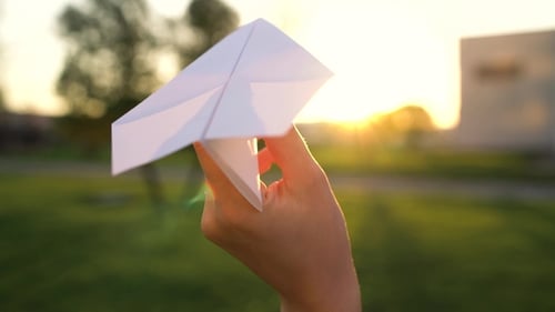 Mano lanza avión de papel contra el fondo del atardecer