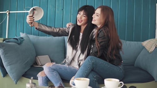 Girlfriends Do Selfie on Mobile Phone Cameras While Sitting in a Cafe