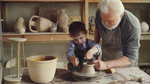 Curious Boy Is Learning Pottery From His Experienced Grandfather in Small Home Studio. Child Is