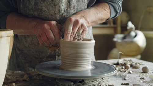 de mains masculines décorant un pot en céramique semi-fini sur le volant de lancer de potier tournant