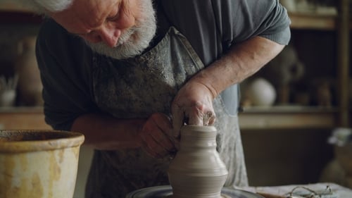 Hard-working Senior Potter Is Wetting Hands in Bowl with Water and Touching Clay Jar