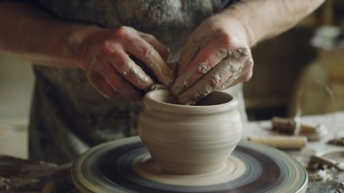 Le potier professionnel fabrique de la vaisselle en argile sur le tour de potier, regardant un pot à moitié fini