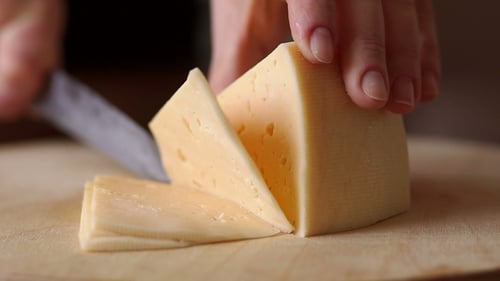 Slicing Wedge of Cheese on Wooden Board