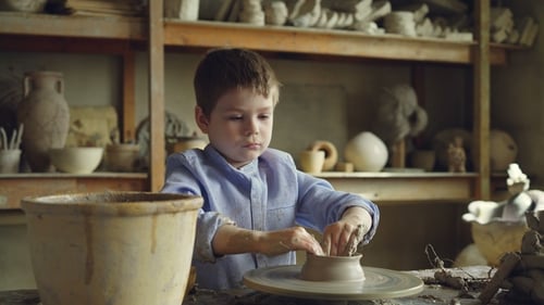 Cute Curious Child Is Making Clay Pot on Spinning Throwing Wheel in Professional Workshop.