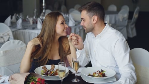 Happy Loving Couple Is Holding Hands, Talking and Kissing During Romantic Dinner in Restaurant