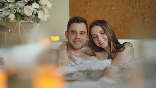 Retrato de jóvenes amantes guapos abrazándose en el jacuzzi, sonriendo y mirando a cámara