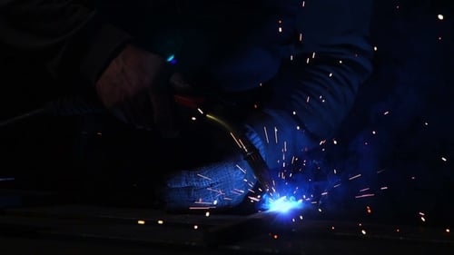 Welder Works in a Mask while Sparks Fly in Different Directions