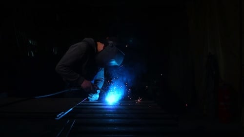 Welder Works in a Mask while Sparks Fly in Different Directions