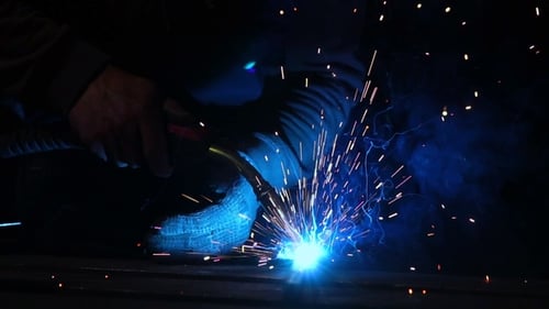 Welder Works in a Mask while Sparks Fly in Different Directions