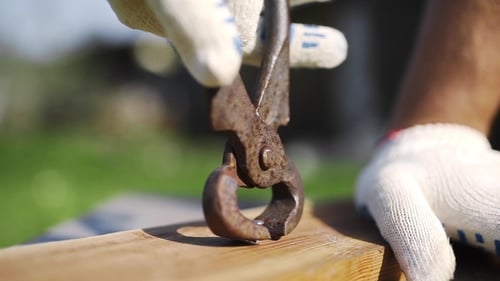 Man in Working Gloves Pulls Out the Hammered Nail From Wood By Rusty Nail Puller Outdoors