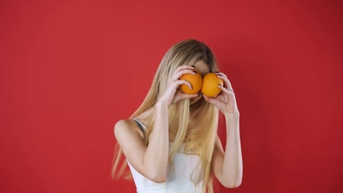 Playful Woman with Oranges on Red Background