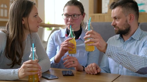 Three Friends Sit in a Cafe, Drink Juice and Have Fun Communicating