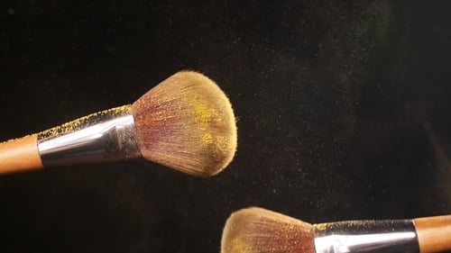 Pinceau cosmétique avec poudre dorée sur fond noir