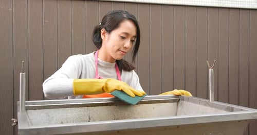 Woman Cleans Metal Container with Sponge and Gloves
