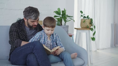 Father and Son Reading a Book on Sofa
