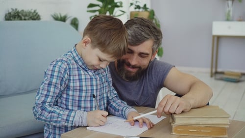 Adorable Child Junior School Student Is Doing Homework Writing in Exercise Book with His Father
