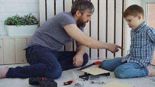 Friendly Father and Small Son Are Talking and Laughing While Doing Construction Work Sitting