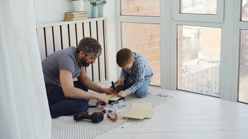 Cute Attentive Boy Is Doing Woodwork Working with Hammer and Pliers While His Experienced Father Is