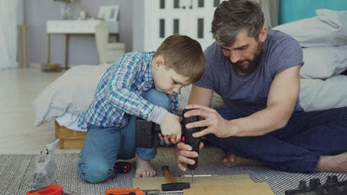 Careful Father Is Teaching His Son To Work with Electric Screwdriver