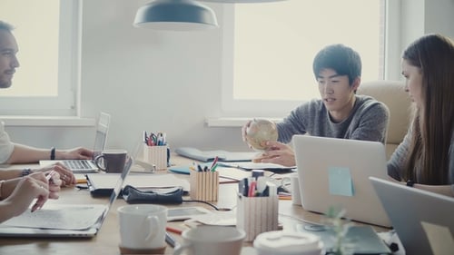 Glücklicher asiatischer Geschäftsmann nimmt einen kleinen Globus, Punkte auf Land bei Multiethnic Office Meeting in